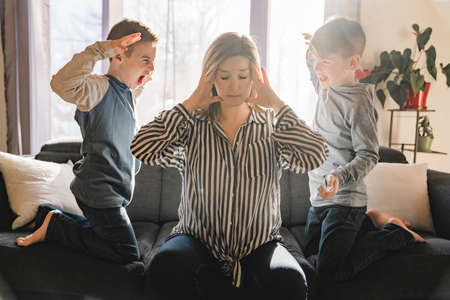 Unhappy Caucasian mom suffer from headache stressed tired by naughty small son playing.