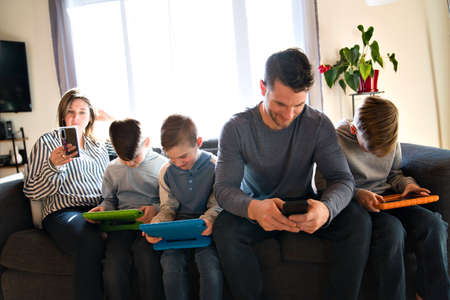 Family of five Relaxing Together On Sofa with technology