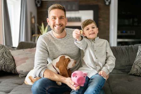 Father or Godfather with Basset dog having fun on the living room At Home puting some money on piggy bankの写真素材