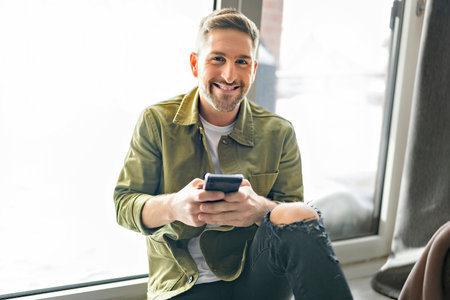 Happy Young Man Relaxing On apartment floor And Looking At Cellphone