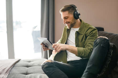 Handsome guy wearing headphones enjoys music sit on the comfortable sofa when using a computer tabletの写真素材