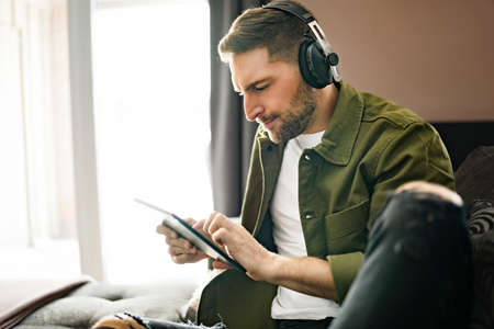 Handsome guy wearing headphones enjoys music sit on the comfortable sofa when using a computer tabletの写真素材