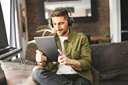 Handsome guy wearing headphones enjoys music sit on the comfortable sofa when using a computer tabletの写真素材
