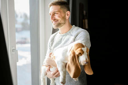 Man Playing With basset Pet Dog At Home close to a window