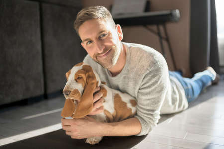 Man Playing With basset Pet Dog At Home on his apartmentの写真素材