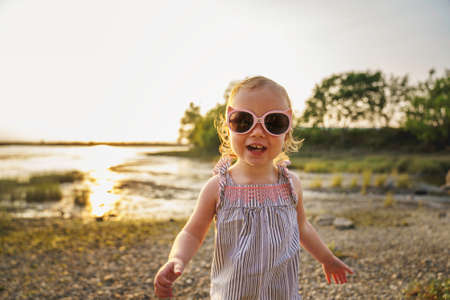 Baby outdoors enjoying nature on the sunset beach with sunglassesの写真素材