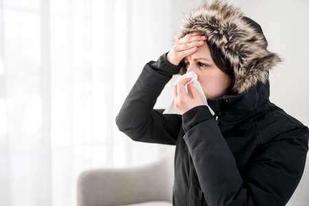 Woman With Warm Clothing Feeling The Cold Inside House on the sofa she having flu and using tissue