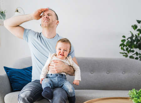 Man holding a screaming baby the father have headacheの写真素材