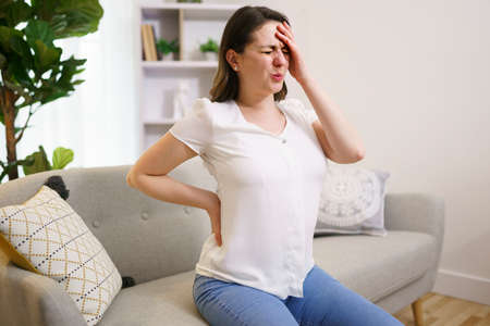 close up of unhappy woman suffering from pain in back or reins at home