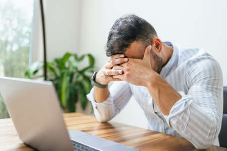 Portrait of a sad and depress mexican businessman working at modern home office with computer laptop