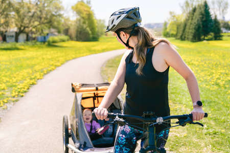 woman riding a bicycle with a baby stroller attached to the bicycle.