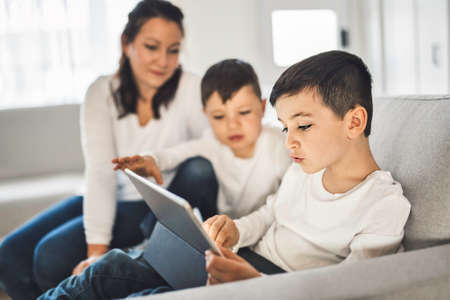 child sitting on couch and looking at a digital tablet while relaxing at home with mother helpの写真素材