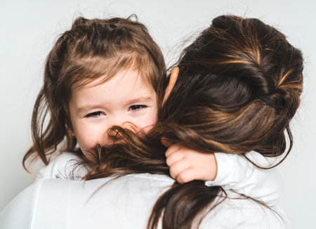 Mother comforting her crying little girl on white