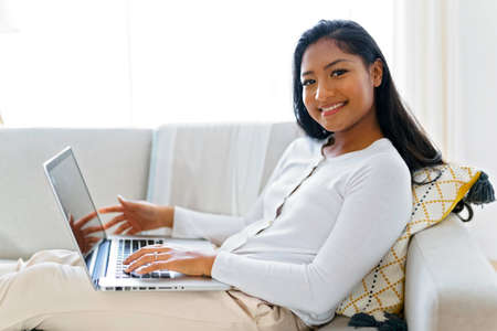 black woman using her laptop on cosy sofa at home