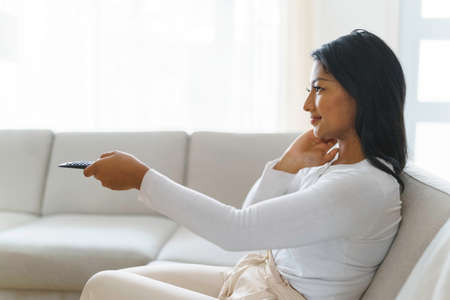 black woman watching television at home sit on sofa