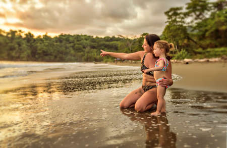 happy family at the beach a mother child daughter having fun at sunsetの写真素材