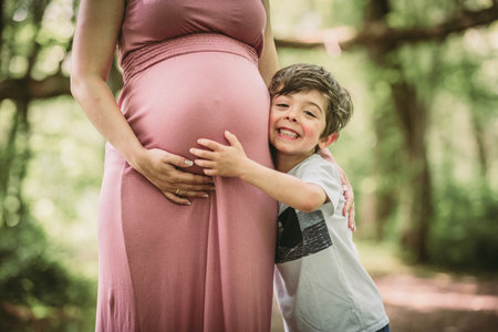 Pregnant woman posing in a green garden with his child boy
