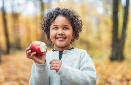 black child girl on maple leaves background holding appleの写真素材