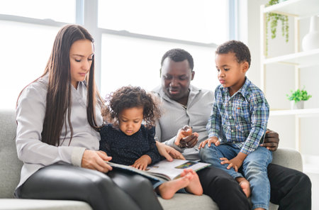 family with boy and girl child posing on photo shooting, sitting on couch and reading bookの写真素材