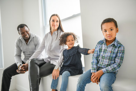 family with boy and girl child posing on photo shooting, sitting close to a windowの写真素材