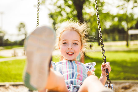 Happy 3 years old girl on a swing. Happy kid on playgroundの写真素材