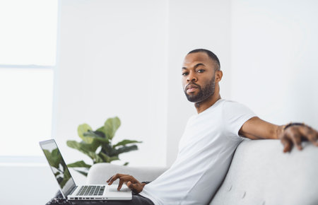 Young happy man on laptop at home A Casual guy sitting on couch in light livingroomの写真素材