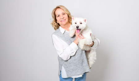 Cheerful retired senior woman with dog and enjoying time with pet on studio whiteの写真素材