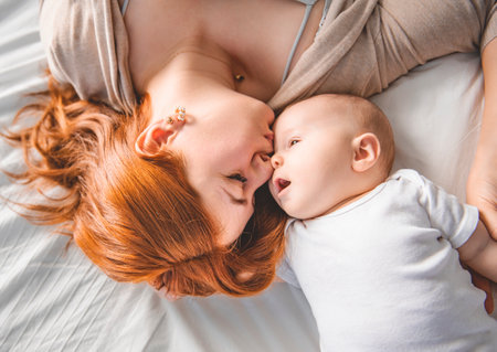 young beautiful mother with a baby boy on the bed at homeの写真素材