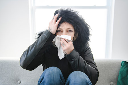 woman sit at home in jackets. The house is very cold. sits on sofa without heating.の写真素材