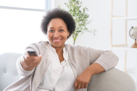 Black woman sitting on sofa at home with remote control