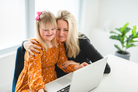 Portrait of beautiful little girl having down syndrome with mother in front of a laptopの写真素材