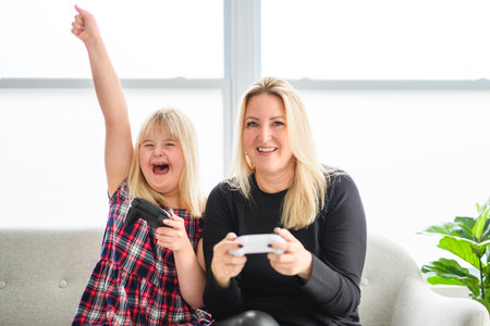 Mother and sweet down syndrome daughter girl at home play video gameの写真素材