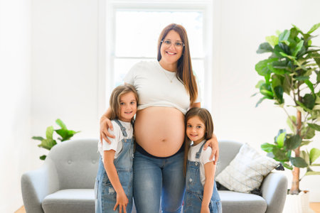 Excited two little daughter with pregnant mom tummy at home