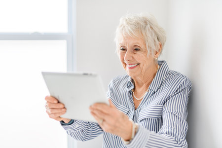 senior lady posing at home portrait close to a window with tabletの写真素材
