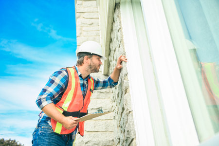 worker man with hard hat inspecting house windowの写真素材