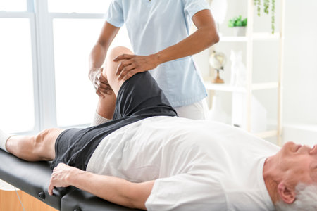 Black physiotherapist helping senior man with in clinic. Elderly man undergoing physiotherapy treatment for injuryの写真素材