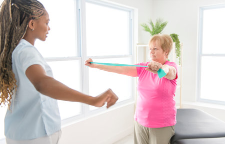 Black physiotherapist helping senior woman in clinic. Elderly woman undergoing physiotherapy treatment for injuryの写真素材