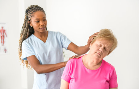 Black physiotherapist helping senior woman in clinic. Elderly woman undergoing physiotherapy treatment for injuryの写真素材