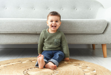 little boy 2 years old sits on bottom of comfortable sofa at home