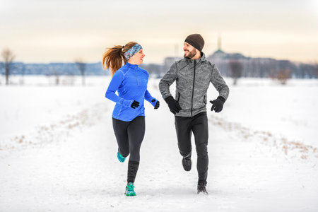 active runner couple jogging together in snowy path in nature.の写真素材