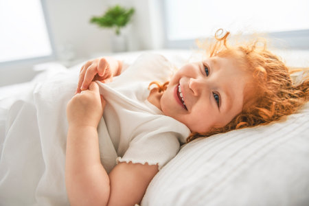 Redhead girl on the bed rests and plays. Cute little girlの写真素材