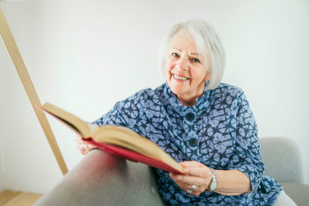 portrait of elderly woman sit on the sofa at home read bookの写真素材