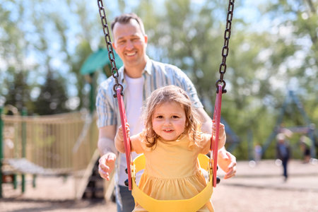 Father Pushes Swings with His Cute Little Daughterの写真素材