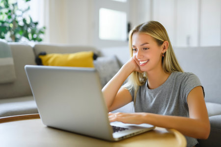 Happy teenager girl online with a laptop in the living room at homeの写真素材