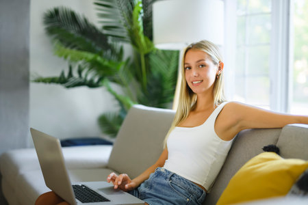 Happy teenager girl online with a laptop in the living room at homeの写真素材