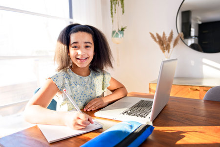 portrait of cute child doing homework on kitchen table with laptopの写真素材