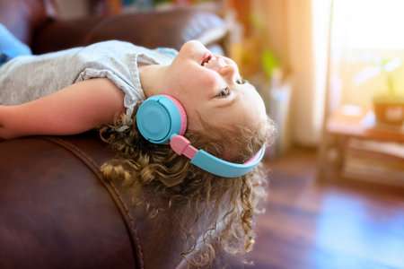 Close up portrait of happy cheerful little girl in grey shirt listening something in headphones and posing at the camera in white roomの写真素材