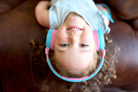 Close up portrait of happy cheerful little girl in grey shirt listening something in headphones and...