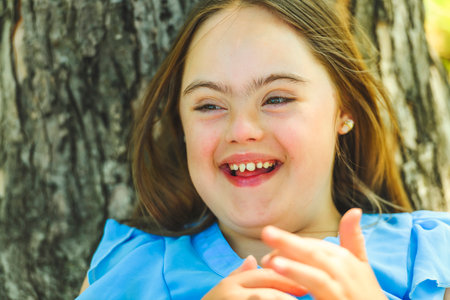 portrait of trisomy 21 child girl outside close to a tree having fun on a parkの写真素材