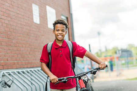 Smiling african american school boy with backpack and bikeの写真素材